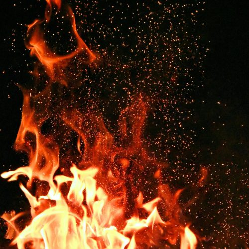 Vivid orange flames and sparks dance against a mysterious black backdrop.